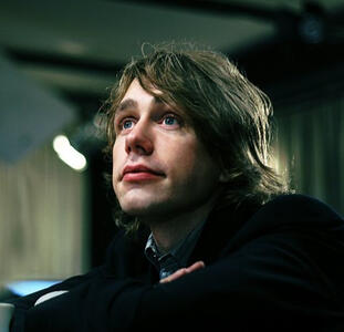 Jonas Bjerre sits with his arms folded on a table and stares into the distance. The photo is from around 2009.