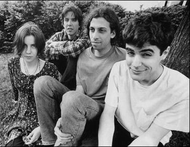 A black and white photo of the four members of the Swirlies in the 90s. They are sitting together on the ground.